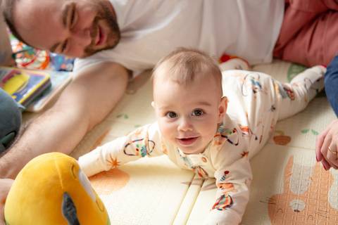 Pai e bebê brincando juntos no tapetinho de atividades, com brinquedos coloridos espalhados ao redor em ensaio de família em SP'