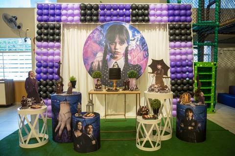 Mesa do bolo ricamente decorada com o tema da Wandinha, com elementos como teias de aranha, velas e cores escuras, em festa infantil no Buffet Vip Kids em São Paulo.'