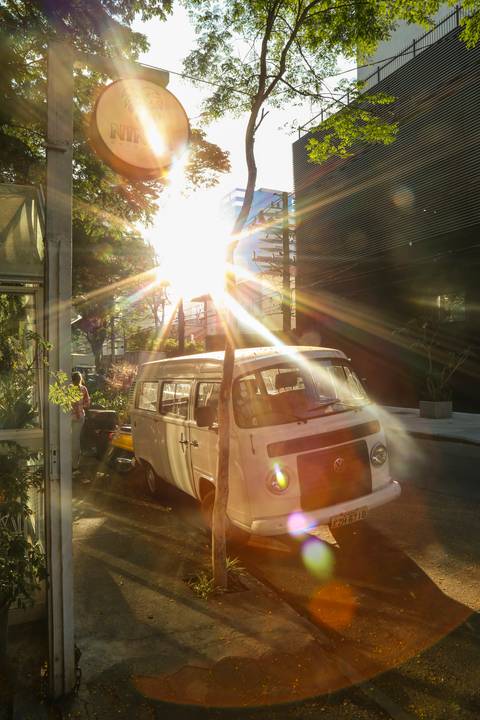Kombi vintage estacionada em frente à floricultura Ninfa Flores, com o sol brilhante ao fundo criando um halo de luz. (reFestança, São Paulo) fotografia Bruno Arita'