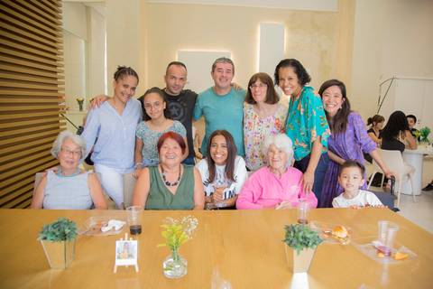 Aniversariante Reiko posando para foto com convidados na mesa do bolo, registrando a presença de amigos e familiares em seu aniversário.'