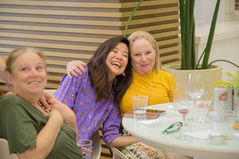 Filha da aniversariante rindo abertamente em conversa com convidados, demonstrando a alegria e o clima descontraído da festa.'