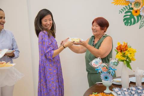 Aniversariante Reiko oferecendo o primeiro pedaço de bolo para sua filha, um gesto de carinho e afeto tradicional em aniversários.'