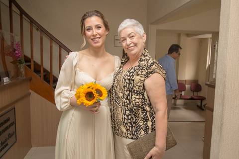 Noiva Ana posando com um buquê de girassóis vibrantes ao lado de sua mãe dentro do 28º Cartório Jardim Paulista, em seu casamento civil'