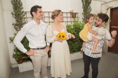 Casal Ana e Leonardo conversando com um convidado que segura uma criança no colo, em um momento descontraído pós-cerimônia'