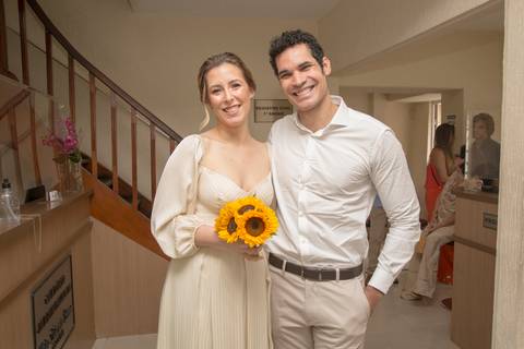 Noivos Ana e Leonardo posando juntos dentro do 28º Cartório Jardim Paulista, a noiva segurando um buquê de girassóis, em seu casamento civil'