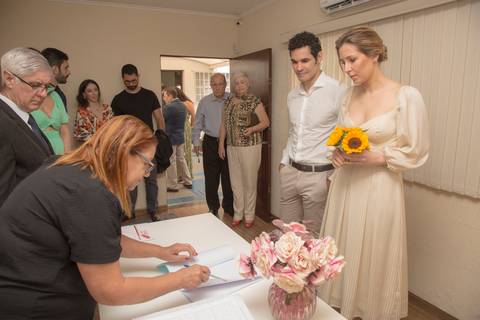 Início da cerimônia de casamento civil no 28º Cartório Jardim Paulista, com convidados reunidos ao redor dos noivos, de frente para a mesa do juiz'