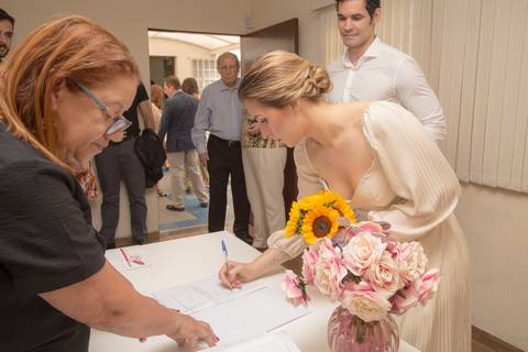 Noiva Ana assinando o documento oficial do casamento civil, enquanto o noivo Leonardo a observa com carinho no 28º Cartório Jardim Paulista'