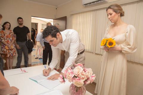 Noivo Leonardo assinando o documento oficial do casamento civil, enquanto a noiva Ana o observa atentamente no 28º Cartório Jardim Paulista'