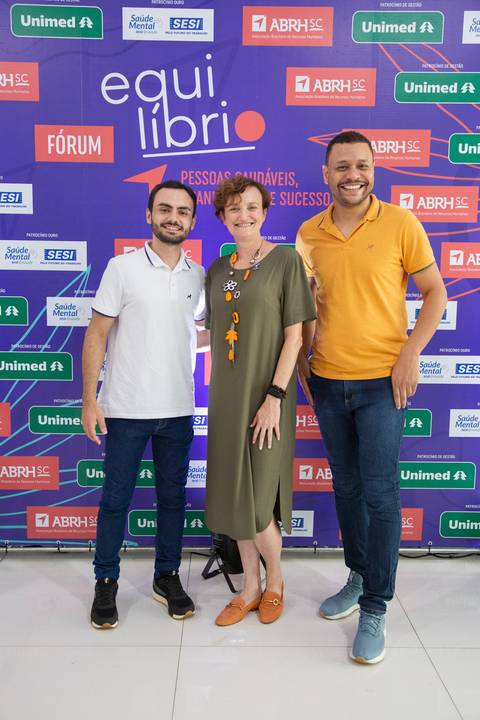 Grupo de participantes do Fórum Equilíbrio da ABRH SC posando sorridentes para foto no painel backdrop. Fotografia Bruno Arita'