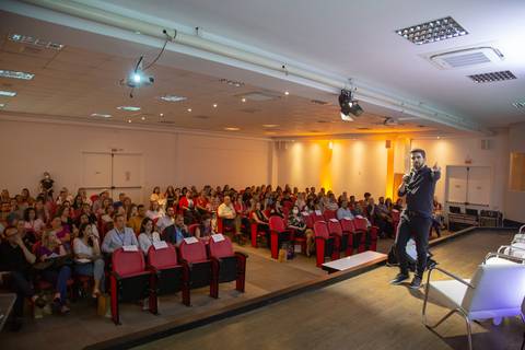 Médico palestrante em primeiro plano no palco do Fórum Equilíbrio da ABRH SC, com o público visível ao fundo, atento à apresentação. Fotografia Bruno Arita'