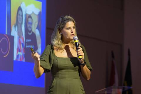 Palestrante mulher em destaque no palco do Fórum Equilíbrio da ABRH SC, gesticulando enquanto fala para a plateia. Fotografia Bruno Arita'