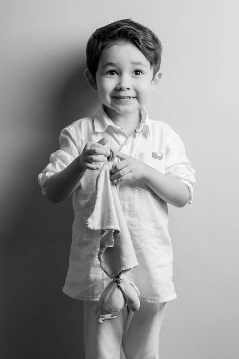 Retrato em preto e branco do filho de 5 anos, segurando carinhosamente seu paninho, com expressão doce e inocente. (Ensaio de Família, São Paulo, Fotógrafo Bruno Arita)'