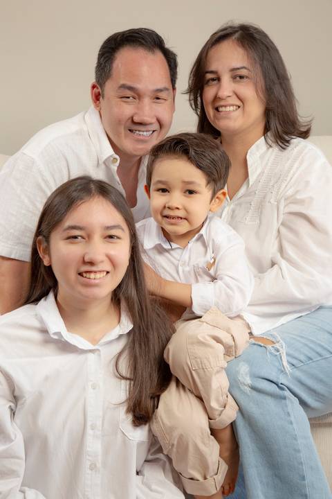 Filha adolescente de camisa branca e calça creme sentada no chão, filho de 5 anos no colo dos pais (camisa social branca e jeans para o pai, camisa branca e jeans para a mãe), com a família reunida no sofá branco. (Ensaio de Família, São Paulo, Fotógrafo '