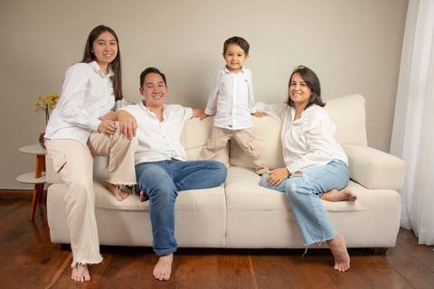 Plano aberto de família no sofá branco: filha adolescente no braço, pai relaxado, filho de 5 anos de pé no sofá, e mãe relaxada, todos sorrindo e descontraídos. (Ensaio de Família, São Paulo, Fotógrafo Bruno Arita)'