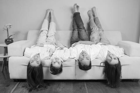 Família (pai, mãe, filha adolescente e filho de 5 anos) sentada de cabeça para baixo no sofá, com os pés na parede, em uma foto divertida em preto e branco que mostra o lado lúdico do lar. (Ensaio de Família, São Paulo, Fotógrafo Bruno Arita)'