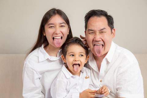Filha adolescente, filho de 5 anos e pai (todos de camisa branca/creme e jeans) mostrando a língua para a câmera em uma foto divertida e espontânea. (Ensaio de Família, São Paulo, Fotógrafo Bruno Arita)'