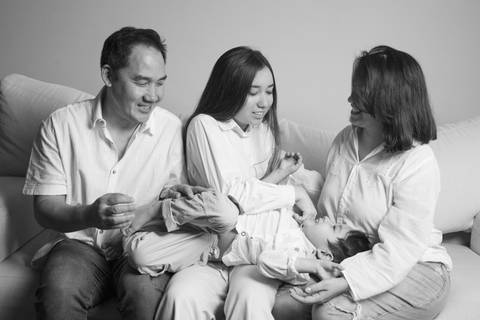 Pai, irmã adolescente e mãe brincando com o filho de 5 anos no colo dos três, em uma foto divertida em preto e branco que captura a alegria e a interação familiar. (Ensaio de Família, São Paulo, Fotógrafo Bruno Arita)'