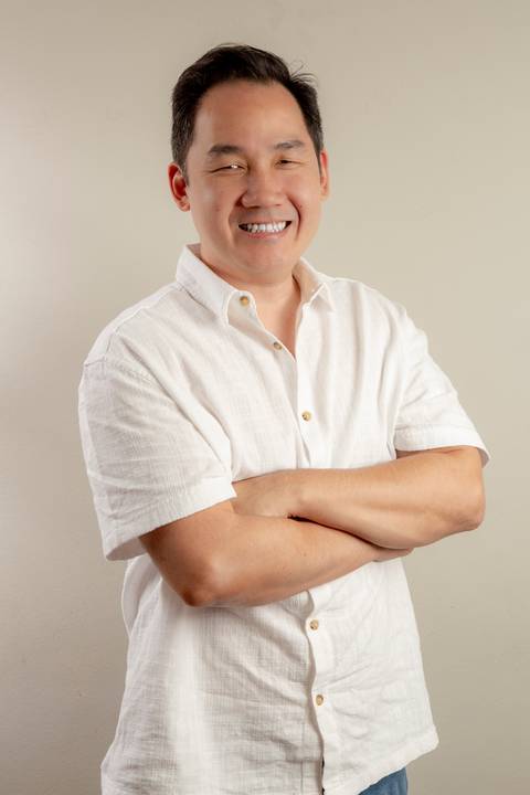 Retrato do pai (camisa social branca e jeans) de braços cruzados, com expressão confiante e acessível. (Ensaio de Família, São Paulo, Fotógrafo Bruno Arita)'