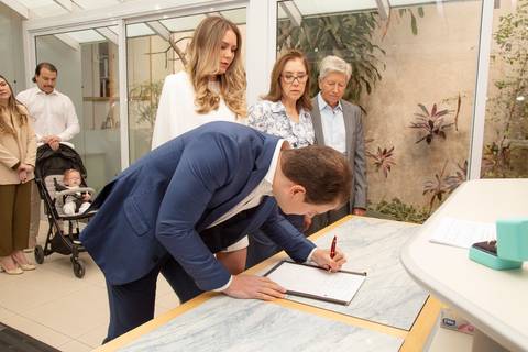 Plano aberto do noivo assinando a certidão, sendo observado com carinho pela noiva e pelos padrinhos. (Casamento Civil, São Paulo, Fotógrafo Bruno Arita)'