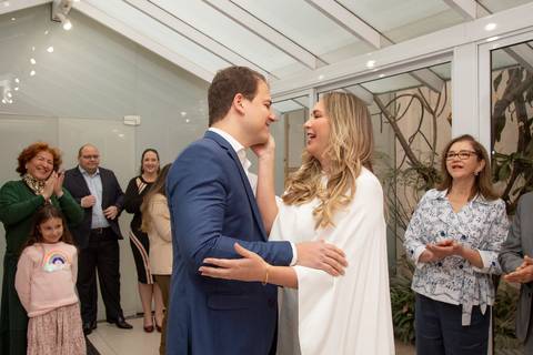 Noivos trocando olhares de felicidade e amor, sorrindo, com os convidados ao fundo após a cerimônia. (Casamento Civil, São Paulo, Fotógrafo Bruno Arita)'