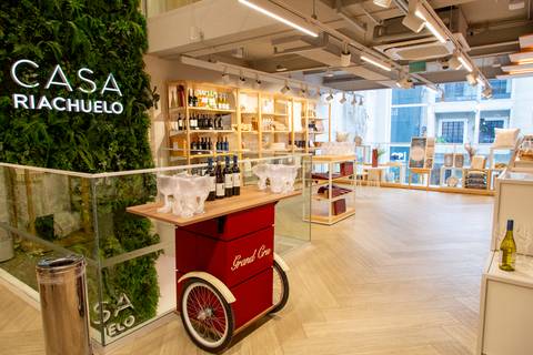 Vista aberta do espaço do evento na Casa Riachuelo, com o letreiro da loja ao fundo e o carrinho vermelho de vinhos da Grand Cru em destaque. (Lançamento Casa Riachuelo, Rua Oscar Freire, São Paulo, Fotos Bruno Arita)'