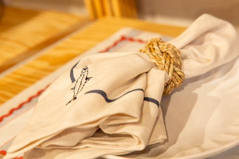 Guardanapo estampado com a identidade visual da nova coleção 'Memórias de Verão' da Casa Riachuelo, repousando sobre um prato. (Lançamento Casa Riachuelo, Rua Oscar Freire, São Paulo, Fotos Bruno Arita)'