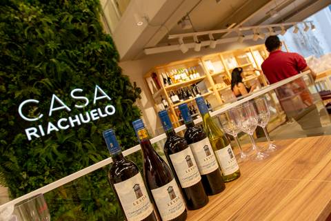 Vinhos e taças em primeiro plano, com o letreiro da Casa Riachuelo visível ao fundo, unindo as marcas no mesmo registro. (Lançamento Casa Riachuelo, Rua Oscar Freire, São Paulo, Fotos Bruno Arita)'