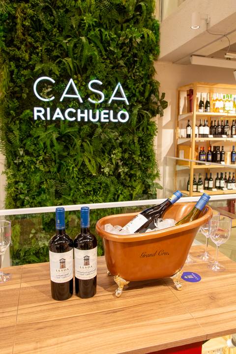 Garrafas de vinho em destaque no balde de gelo da Grand Cru, com o letreiro da Casa Riachuelo ao fundo, unindo as marcas visualmente. (Lançamento Casa Riachuelo, Rua Oscar Freire, São Paulo, Fotos Bruno Arita)'