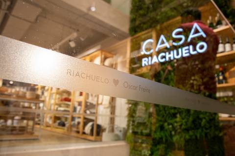 Vidro com a gravura 'Riachuelo Oscar Freire' em primeiro plano, com o letreiro da Casa Riachuelo ao fundo, contextualizando o local do evento. (Lançamento Casa Riachuelo, Rua Oscar Freire, São Paulo, Fotos Bruno Arita)'