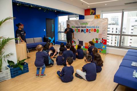 Crianças sentadas na área de brincadeiras, atentas e envolvidas, ouvindo o recreador, em um momento de contação de histórias ou instruções. (Evento Plurix, São Paulo, Fotógrafo Bruno Arita)'