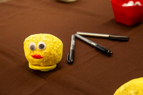Mesa de oficina com materiais para montar a 'cabeça de grama', incluindo canetas e um boneco amarelo pronto com olhos e boca, incentivando a criatividade das crianças. (Evento Plurix, São Paulo, Fotógrafo Bruno Arita)'
