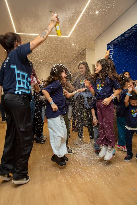 Crianças pulando e dançando, com a recreadora jogando espuma colorida para o alto, em um momento de euforia e diversão. (Evento Plurix, São Paulo, Fotógrafo Bruno Arita)'