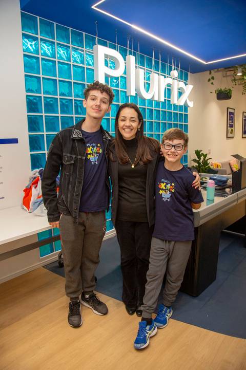 Mãe e seus dois filhos posando para uma foto em grupo, com o logo da Plurix ao fundo, reforçando o pertencimento corporativo. (Evento Plurix, São Paulo, Fotógrafo Bruno Arita)'