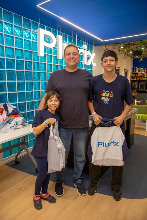 Pai e seus dois filhos posando para uma foto em grupo, com o logo da Plurix ao fundo, celebrando o Dia das Crianças 2025. (Evento Plurix, São Paulo, Fotógrafo Bruno Arita)'