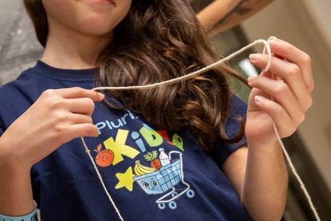 Criança vestindo camiseta Plurix Kids, sorrindo e brincando em um desafio de barbante, em uma atividade de movimento e coordenação. (Evento Plurix, São Paulo, Fotógrafo Bruno Arita)'