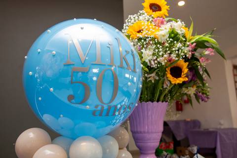 Balão dourado com o número 50, referente ao aniversário de Miki, com um arranjo de flores ao lado. (Aniversário em Dobro, Nanako, São Paulo, Fotógrafo Bruno Arita)'