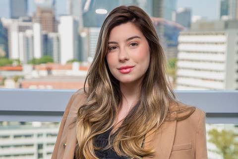 Retrato de busto de Mulher em frente a uma janela com vista para São Paulo, com blazer nos ombros, transmitindo credibilidade profissional. (Retrato Corporativo, São Paulo, Fotógrafo Bruno Arita)'