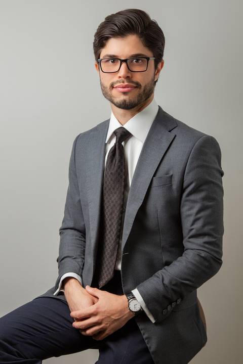 Retrato corporativo de Homem (óculos, terno cinza, gravata preta) com olhar sério e postura confiante, em fundo neutro. (Retratos Corporativos, São Paulo, Fotógrafo Bruno Arita)'