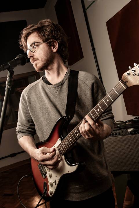 Guitarrista Ivan Lucchini tocando em plano levemente inclinado com olhar lateral, utilizando paleta de cor amarelada. (Banda Madressilva, Ensaio Musical, Fotos Bruno Arita)'