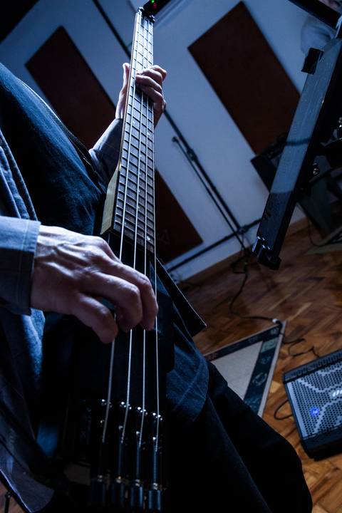 Plano fechado no baixo sendo tocado, utilizando a mesma luz de alto contraste e cor azulada da foto anterior. (Banda Madressilva, Ensaio Musical, Fotos Bruno Arita)'