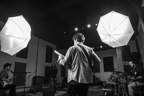 Foto de making of (preto e branco) do baixista, com foco nas costas e luzes brancas iluminando a cena, mostrando o equipamento de estúdio. (Banda Madressilva, Ensaio Musical, Fotos Bruno Arita)'