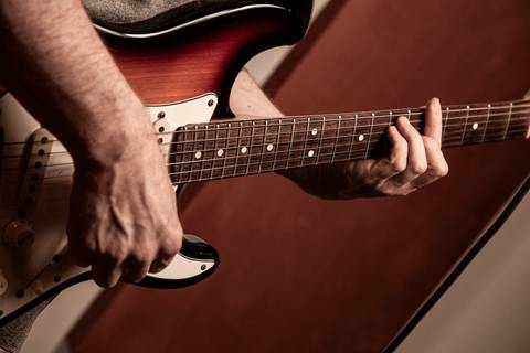 Plano fechado e rústico na guitarra sendo tocada, com paleta de cor mais amarelada. (Banda Madressilva, Ensaio Musical, Fotos Bruno Arita)'
