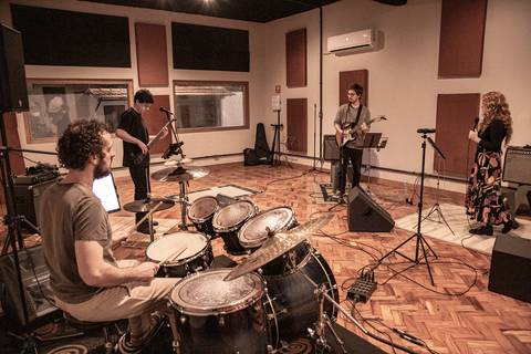 Plano aberto de toda a banda Madressilva ensaiando no estúdio, com paleta de cor amarelada e baixo contraste, em edição artística autoral. (Banda Madressilva, Ensaio Musical, Fotos Bruno Arita)'