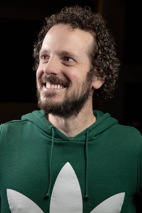 Plano fechado do baterista Bruno Pigat, com olhar lateral, em retrato divertido e amigável, com paleta de cor normal. (Banda Madressilva, Ensaio Musical, Fotos Bruno Arita)'