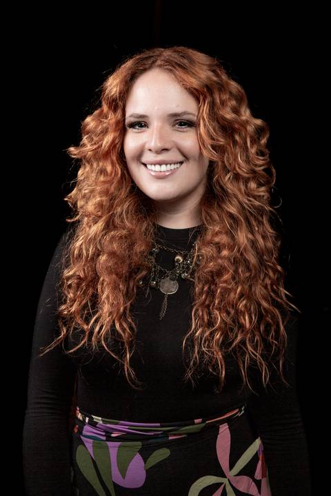 Retrato da vocalista Agnes Gomes (cabelos ruivos, blusa preta), sorrindo em pose natural, utilizando paleta de cor normal. (Banda Madressilva, Ensaio Musical, Fotos Bruno Arita)'