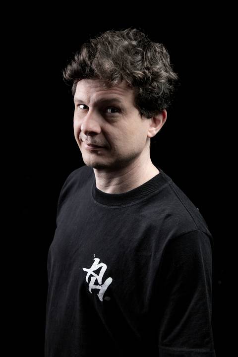 Retrato do baixista Marco Augusto em paleta normal, olhando para a câmera com olhar curioso e divertido. (Banda Madressilva, Ensaio Musical, Fotos Bruno Arita)'