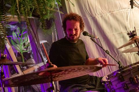 Baterista Bruno Pigat, da Banda Madressilva, em destaque, tocando com expressão clássica de músico durante a apresentação final. (Ninfa Flores, São Paulo, Fotos Bruno Arita)'