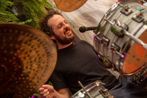Baterista Bruno Pigat, da Banda Madressilva, tocando e sorrindo, transmitindo a energia contagiante da banda. (Ninfa Flores, São Paulo, Fotos Bruno Arita)'