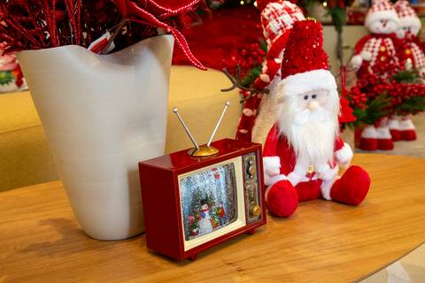Plano detalhe da decoração de Natal com mini TV vermelha (simulando globo de neve) e um Papai Noel de pelúcia sobre mesa de centro de madeira. (Westwing Moema, São Paulo, Fotos Bruno Arita)'