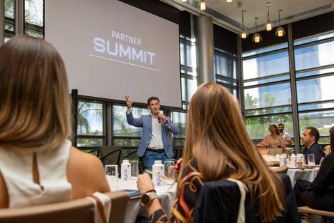 Contra-plongée com participantes em primeiro plano assistindo e anfitrião da Partner PSE ao fundo discursando. (Grand Hyatt SP, Evento Corporativo, Fotos Bruno Arita)'